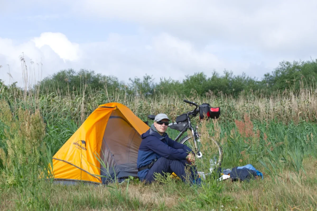 Ja siedzący na trawie przed namiotem a obok stoi rower