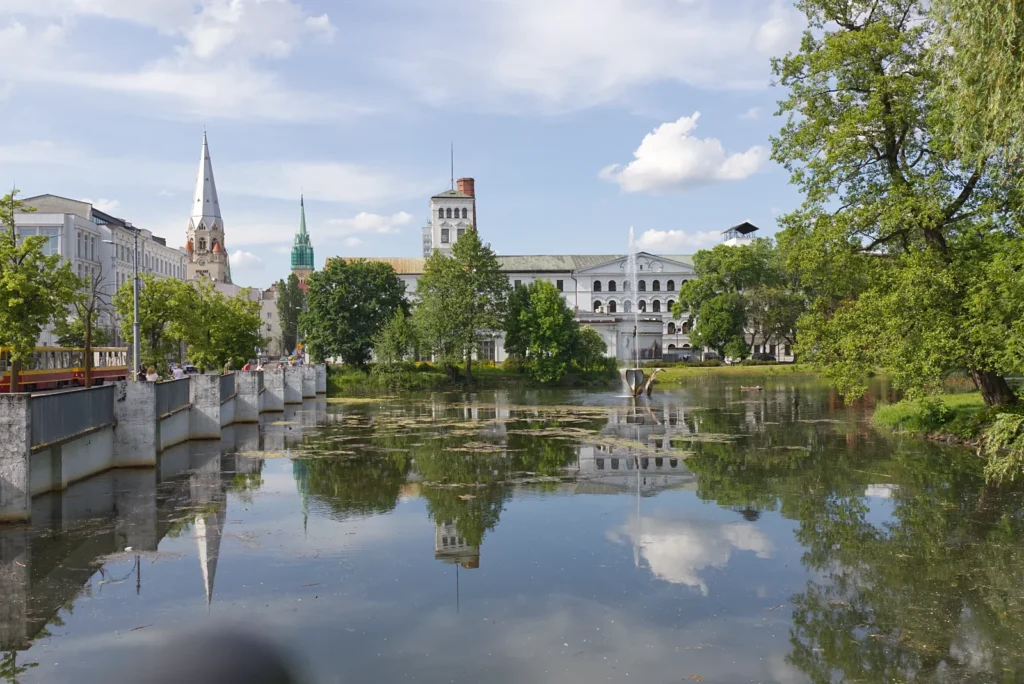 Staw w parku miejskim w mieście Łódź i odbijające się drzewa i budynki w tafli wody