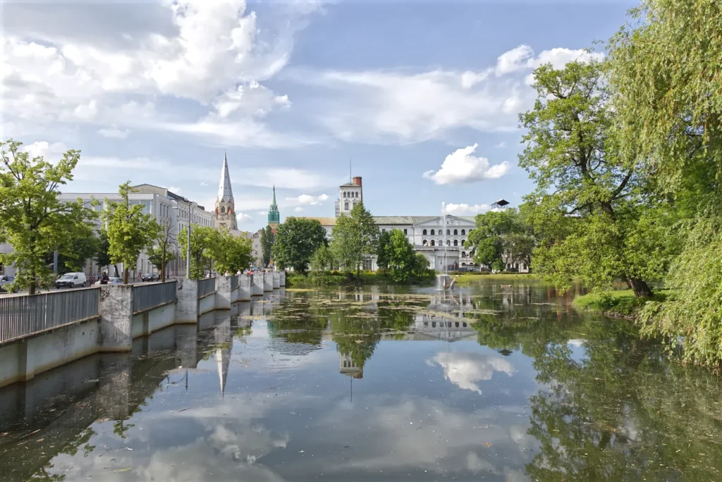 Staw w parku miejskim w mieście Łódź i odbijające się drzewa i budynki w tafli wody