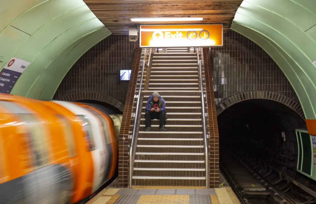 Mężczyzna siedzący na schodach w metrze i metro odjeżdżające, na które się spóźnił